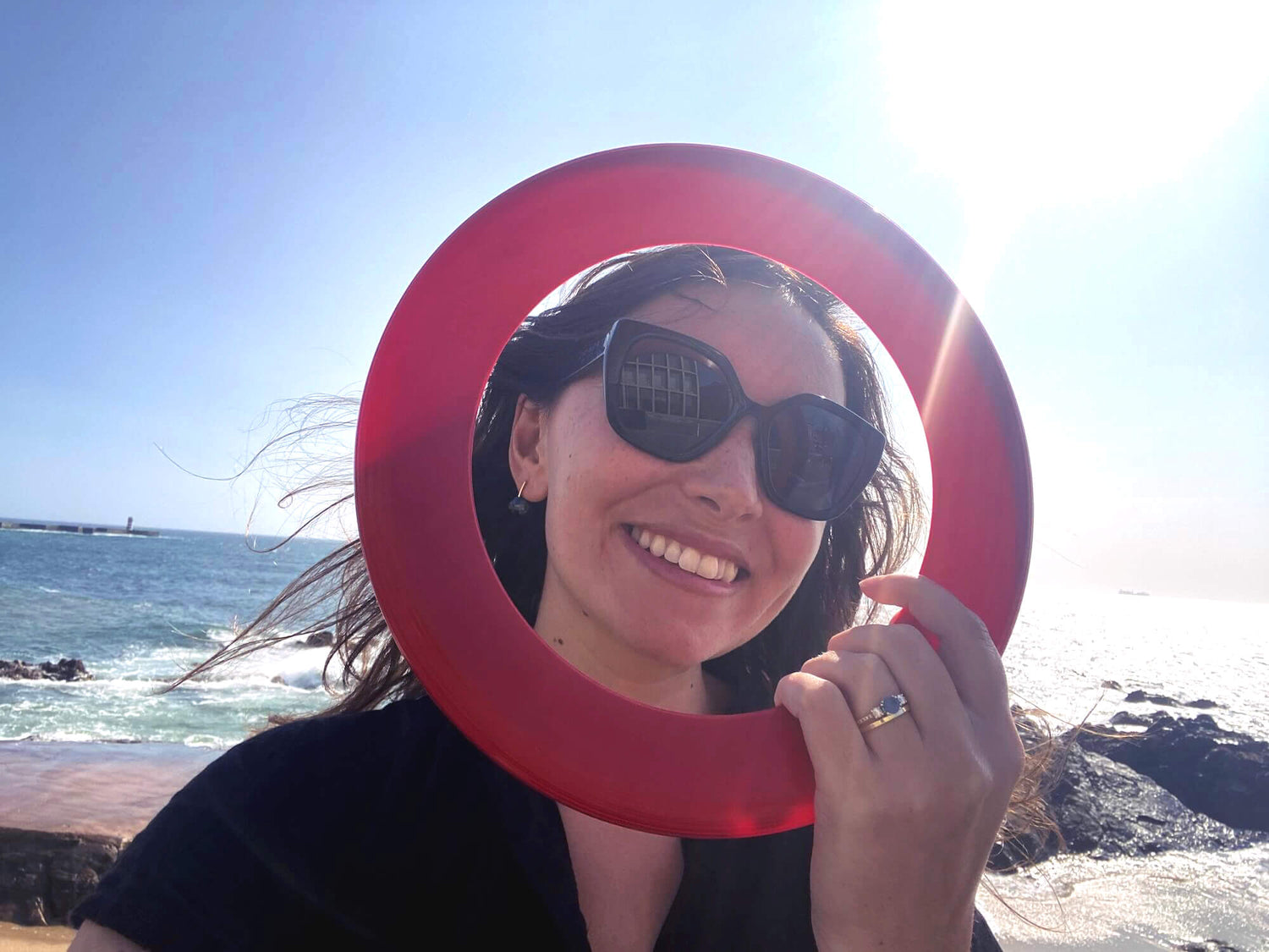 Marianne holding a red First-N-Ten ring against a sunny beach background